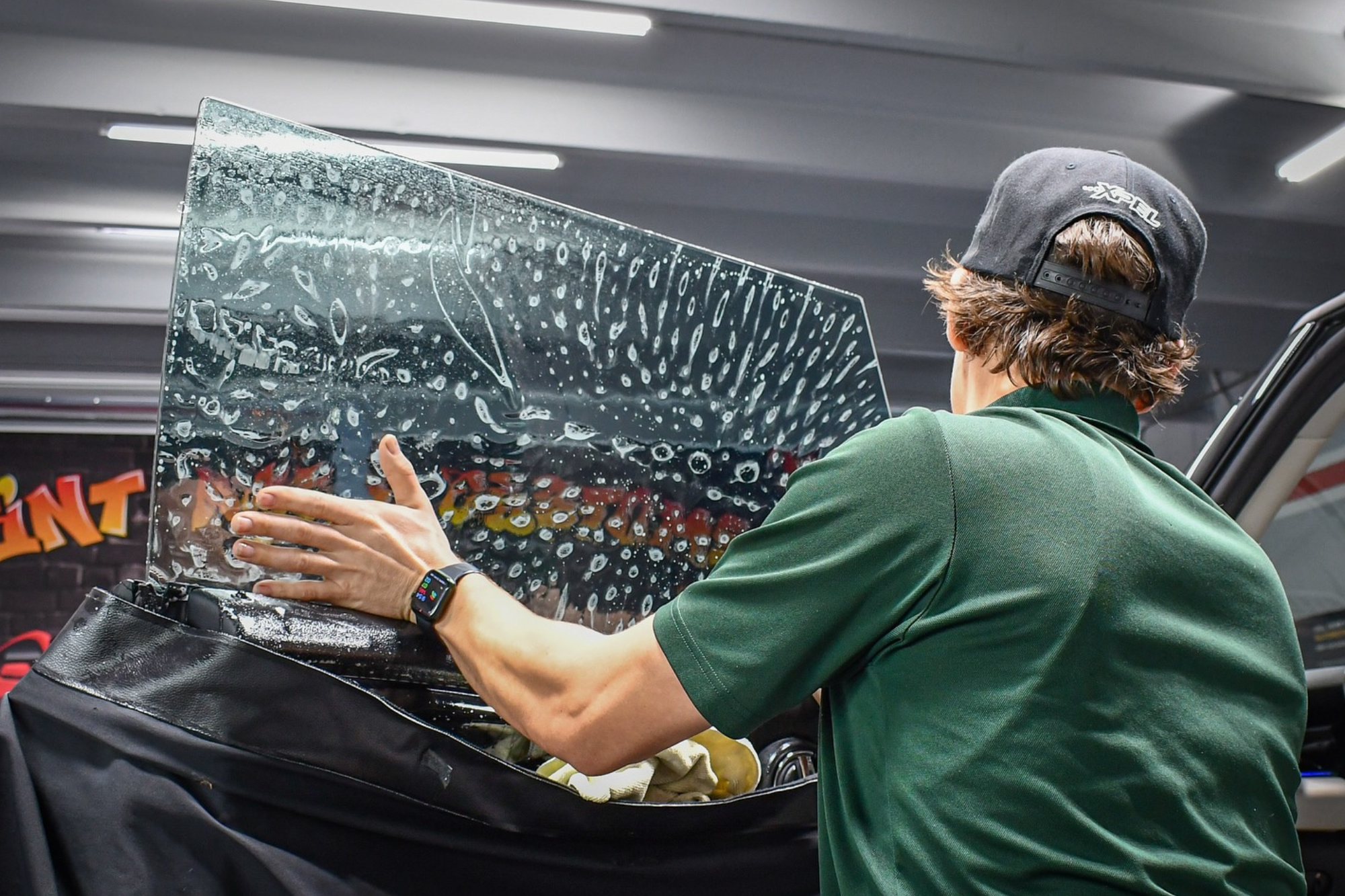 A man carefully places a glass panel on a car, part of the window tinting process for improved aesthetics and comfort.