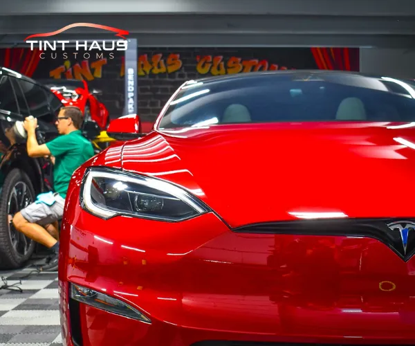 A close-up of a vibrant red electric sedan being polished by a technician in a specialized automotive detailing studio.