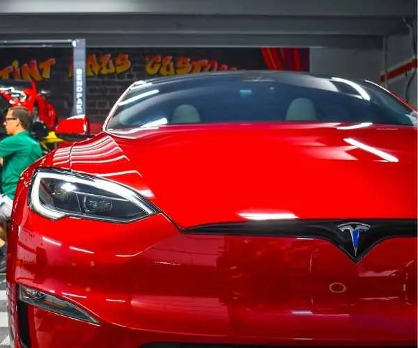applying window tinting film to the side window of a red Tesla sports car inside a professional auto styling shop